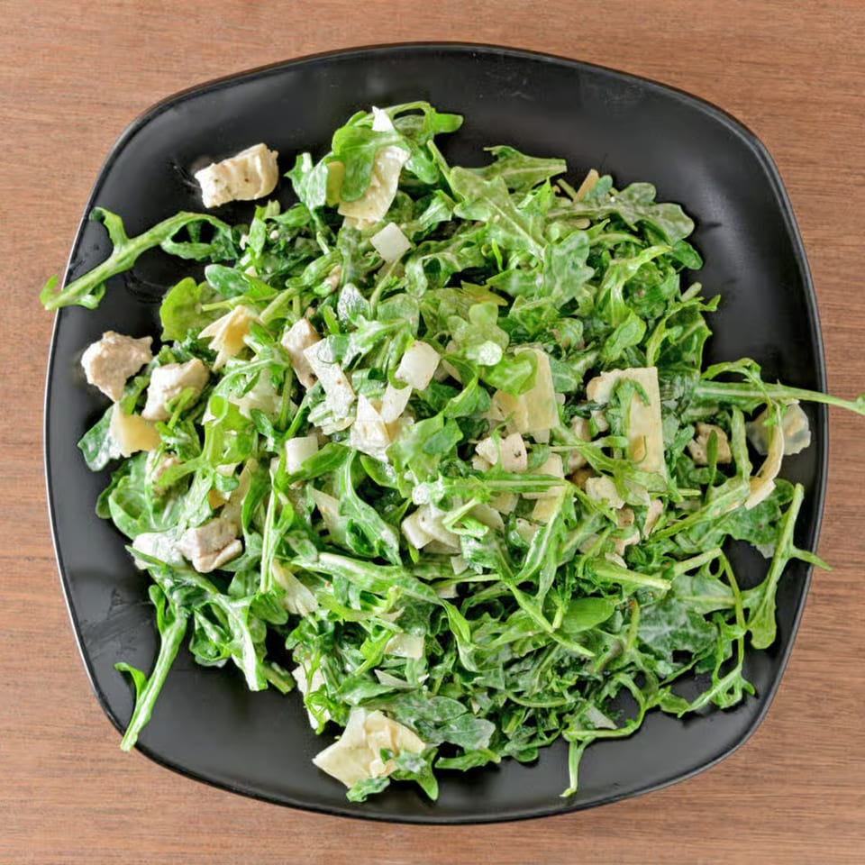 A black plate filled with a fresh arugula salad, topped with artichoke hearts and a creamy dressing.