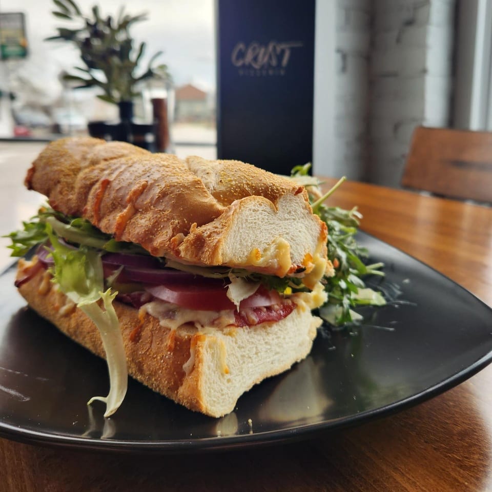 A large, crusty baguette sandwich filled with meat, cheese, lettuce, and tomatoes, served with a side salad.