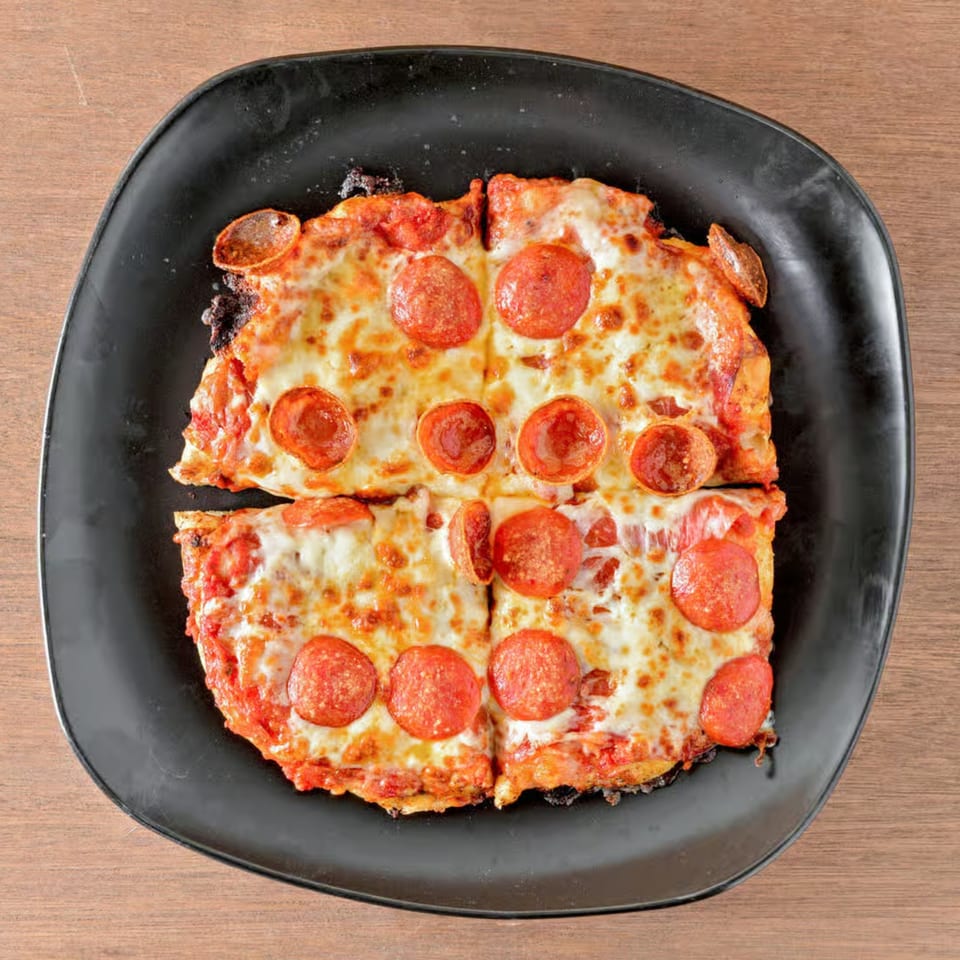 Four square slices of Crust Pizzeria pepperoni pizza on a black plate, viewed from above.