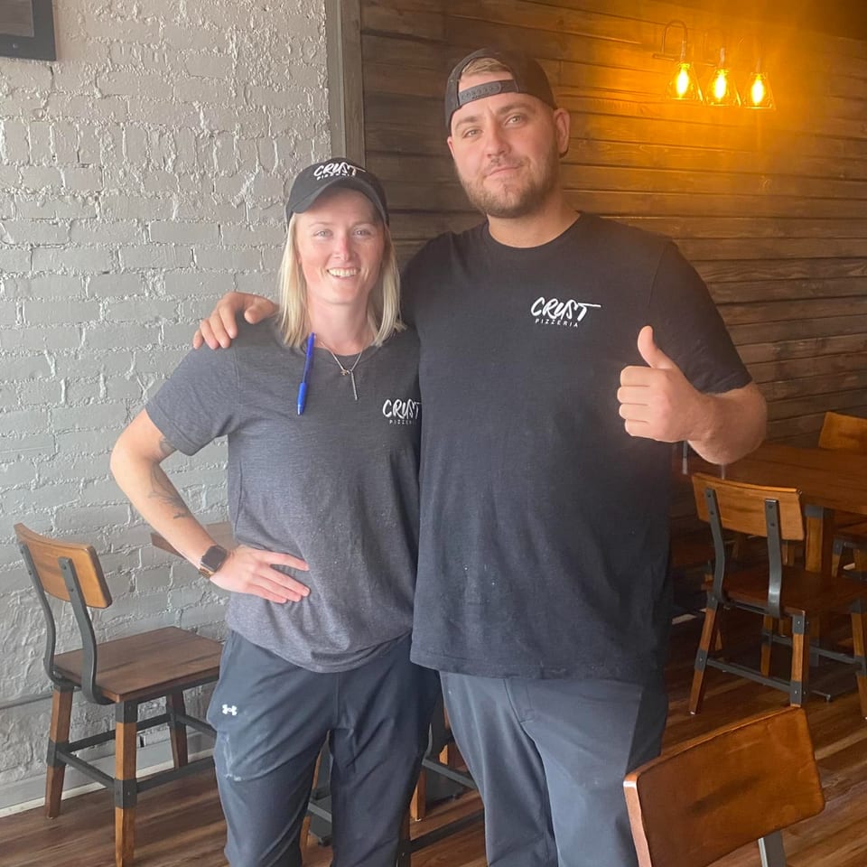 Two Crust Pizzeria staff members, a woman and a man, smiling in the restaurant dining area.