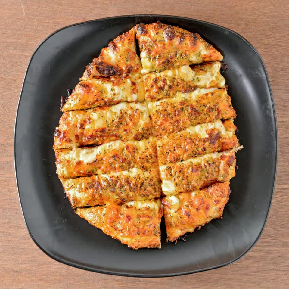 Crust Pizzeria's cheesy garlic bread, cut into strips and served on a black rectangular plate.