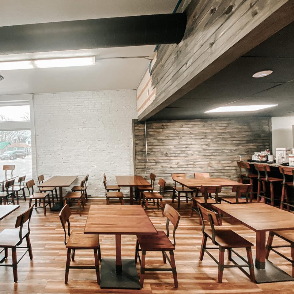 Interior of Crust Pizzeria with wooden tables and chairs, white brick wall, and a wooden accent wall.