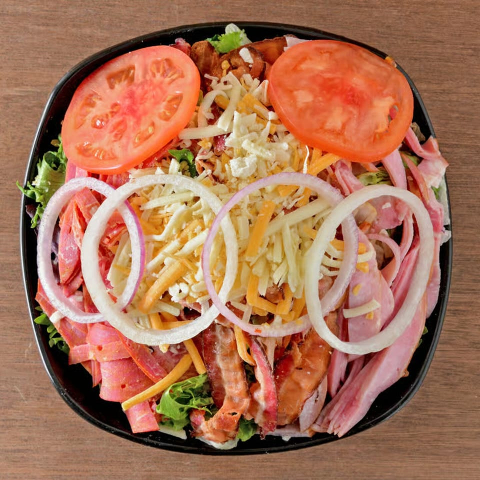 A large salad with ham, salami, bacon, cheese, tomatoes, and onion rings.