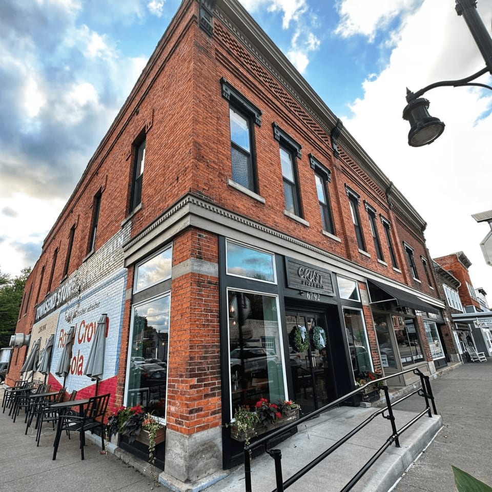 Crust Pizzeria's brick building with outdoor seating and a Royal Crown Cola mural on the side.